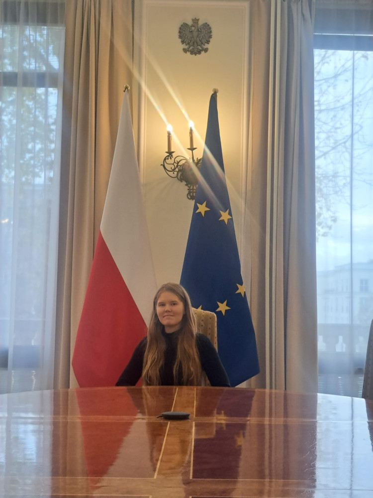 Aleksandra Pesta siedzi na tle flag