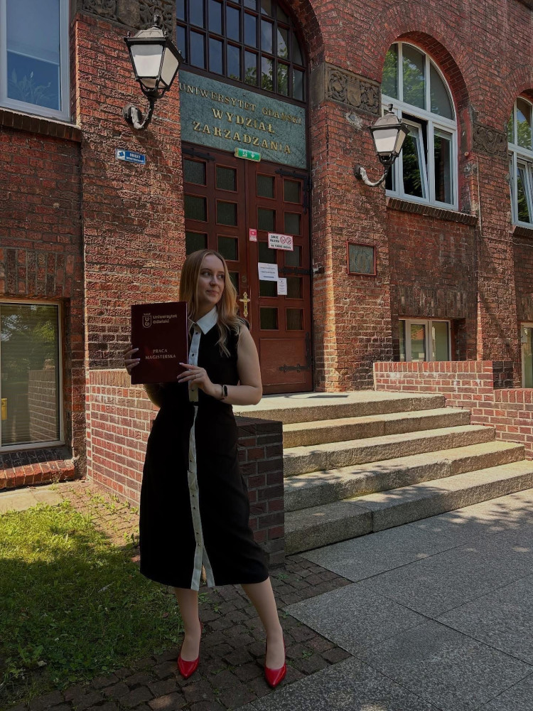 Sara Król przed budynkiem WZR UG prezentuje swoją pracę magisterską